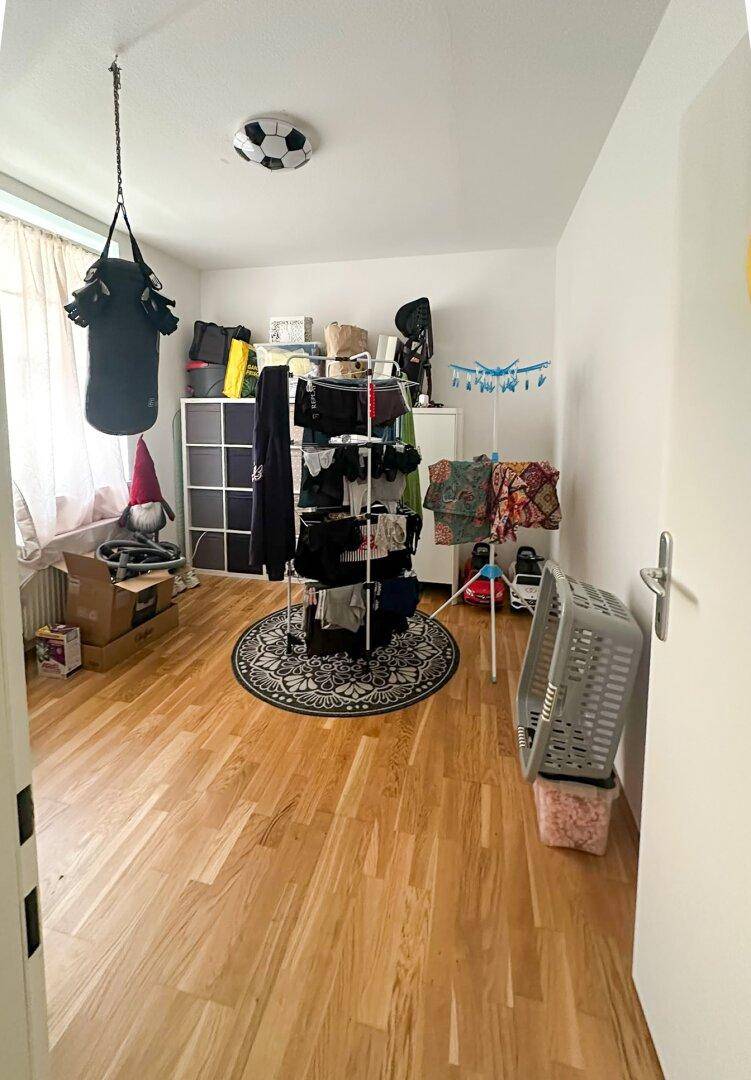 Zimmer mit Holzboden, Wäscheständer und verschiedenen Aufbewahrungsboxen.