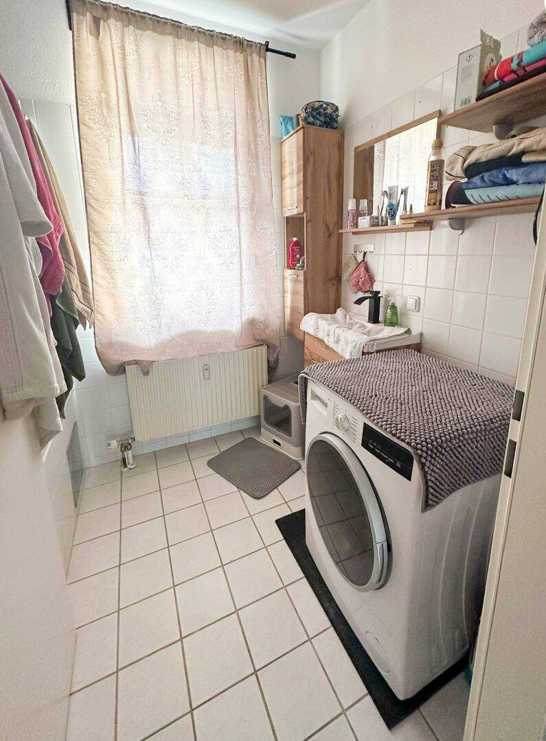 Badezimmer mit weißen Fliesen, Waschmaschine und Fenster für Tageslicht.