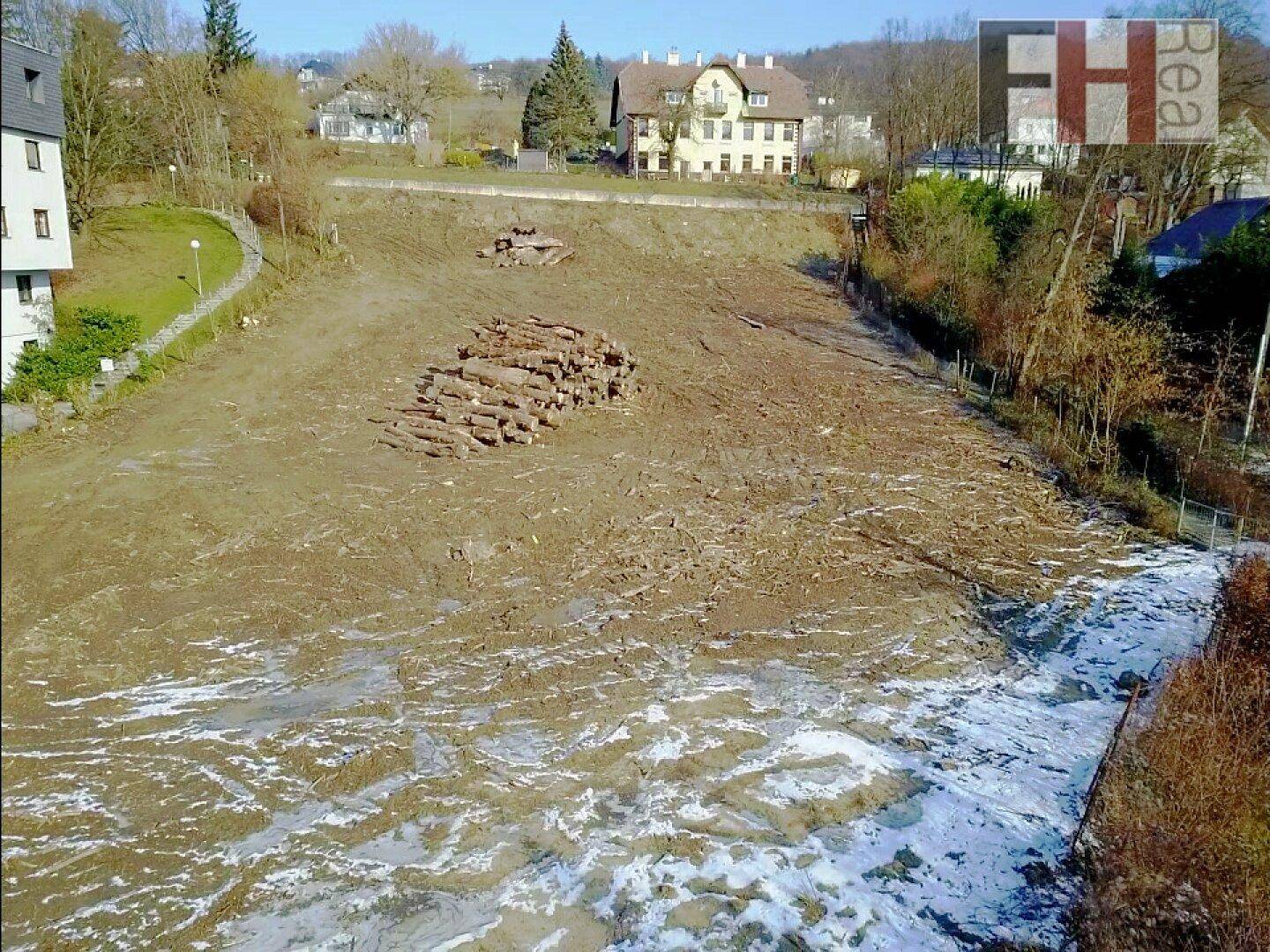 Übersicht des geräumten Grundstücks mit Holzstapeln und Spuren von Baufahrzeugen im Schnee.