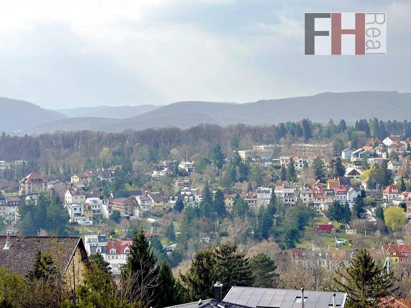 Panoramablick über eine dicht besiedelte Ortschaft in einer hügeligen, bewaldeten Landschaft.