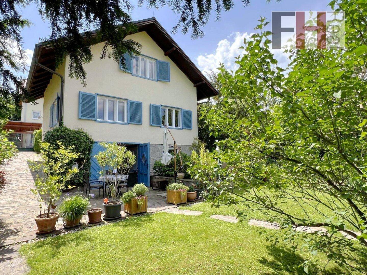 Seitlicher Blick auf das Haus mit blauen Fensterläden und einem gepflegten Gartenbereich mit Terrasse.