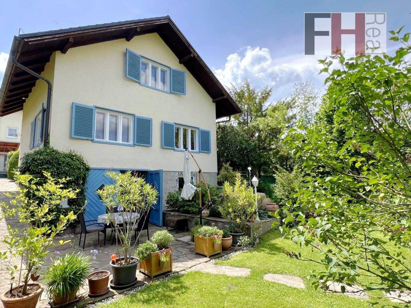 Haus mit blauen Fensterläden und einer einladenden Terrasse, die in den weitläufigen Garten übergeht.