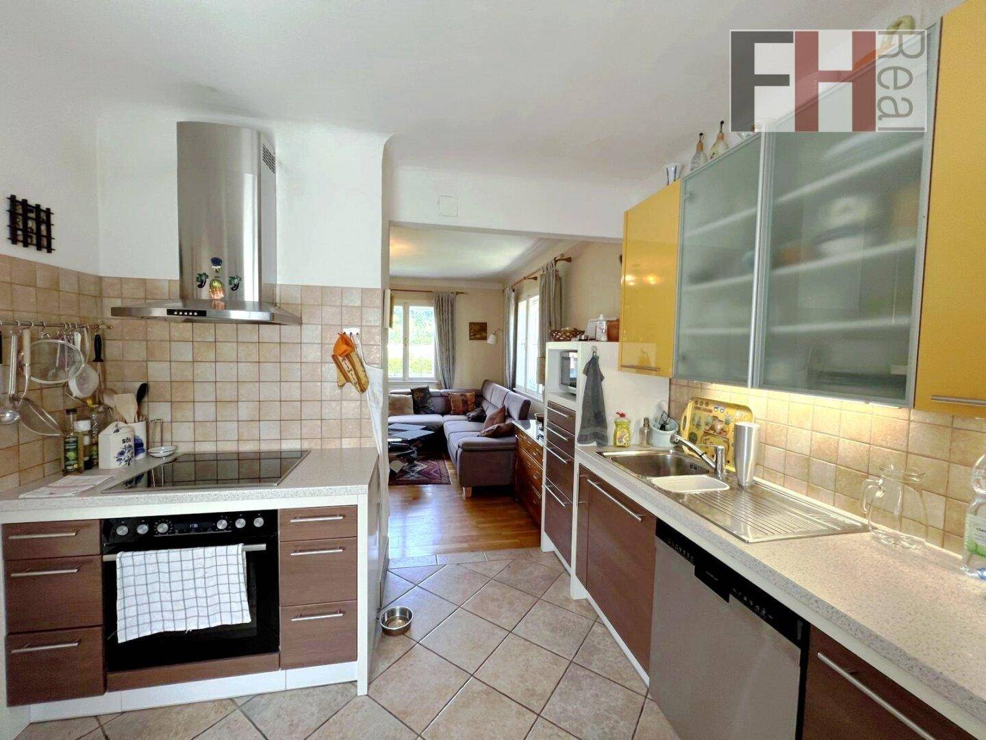 Funktionale Küche mit Fliesenboden, modernen Geräten und Blick in den angrenzenden Wohnbereich.