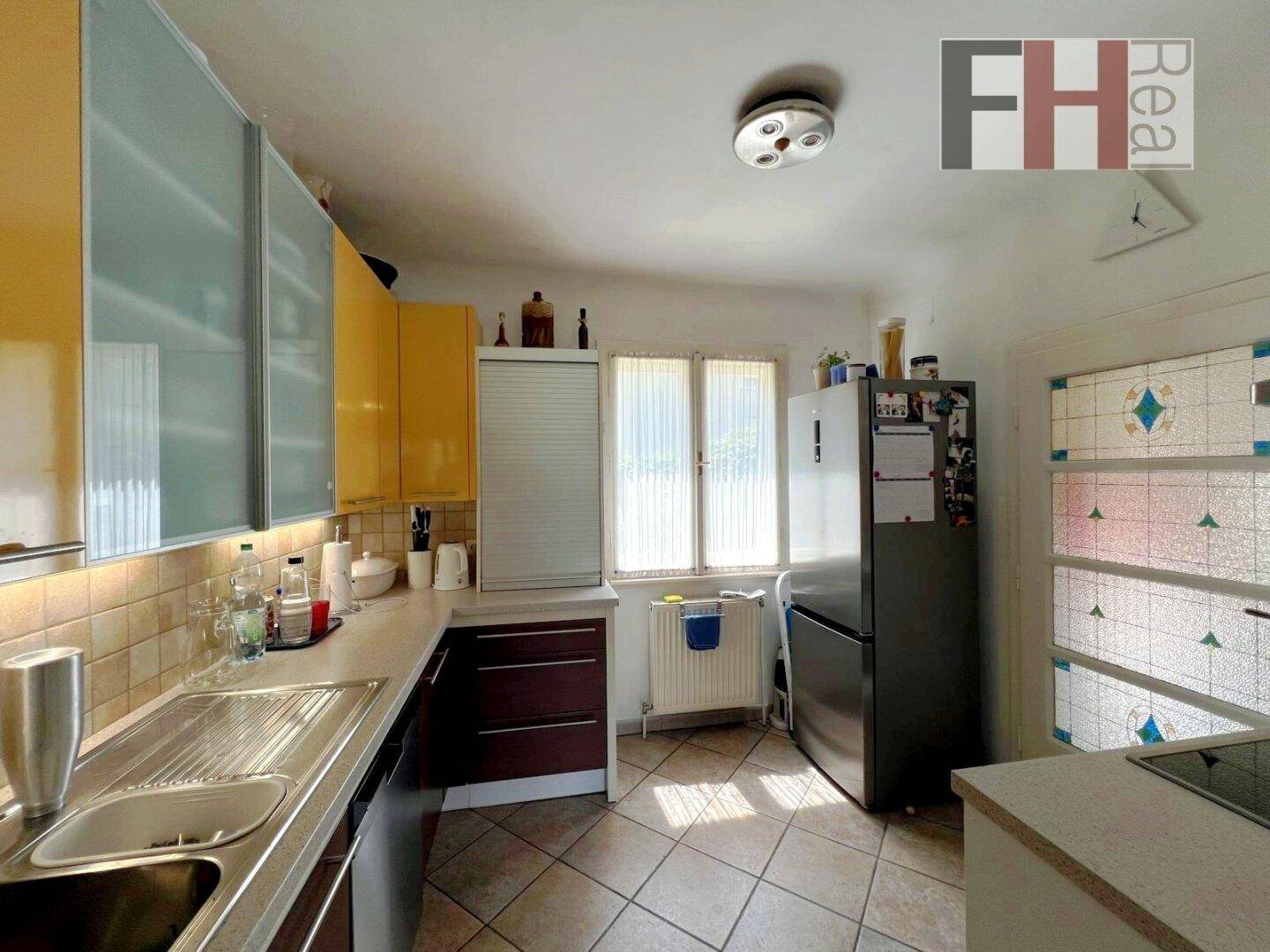 Helle Küche mit Fliesenboden, gelben Oberschränken und einem Fenster für natürliches Licht.