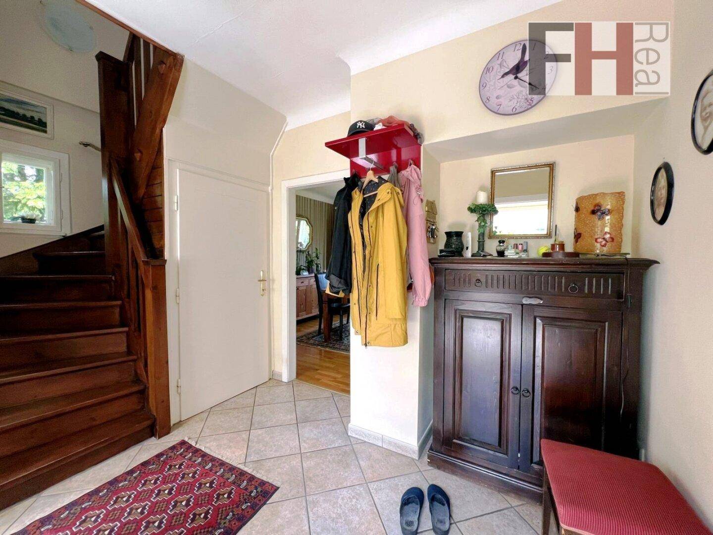 Eingangsbereich mit Fliesenboden, Garderobe und einer Holztreppe, die in die oberen Stockwerke führt.