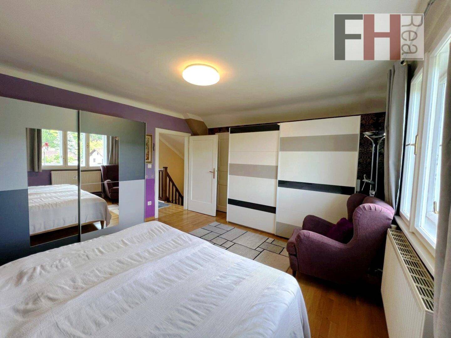 Schlafzimmer mit großem Bett, Spiegelschränken und Zugang zu einer Treppe, hell und funktional eingerichtet.