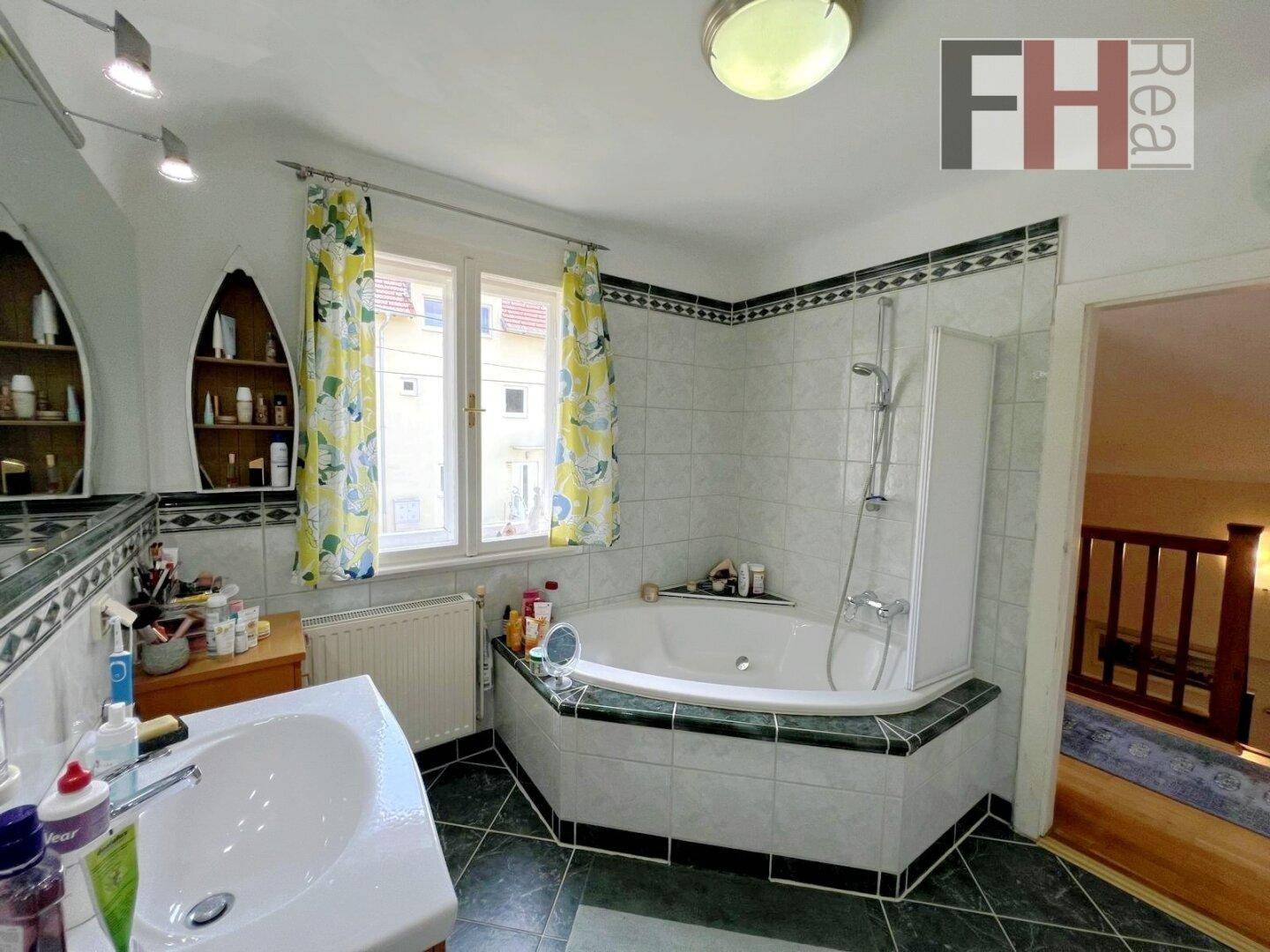 Badezimmer mit Eckbadewanne, Dusche, Waschbecken und Fenster für natürliche Belüftung.