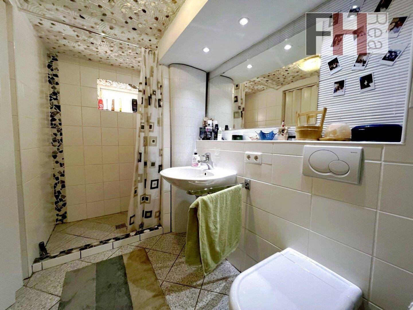 Badezimmer mit Duschbereich, Waschbecken, Toilette und einem großen Spiegel, funktional und hell gefliest.