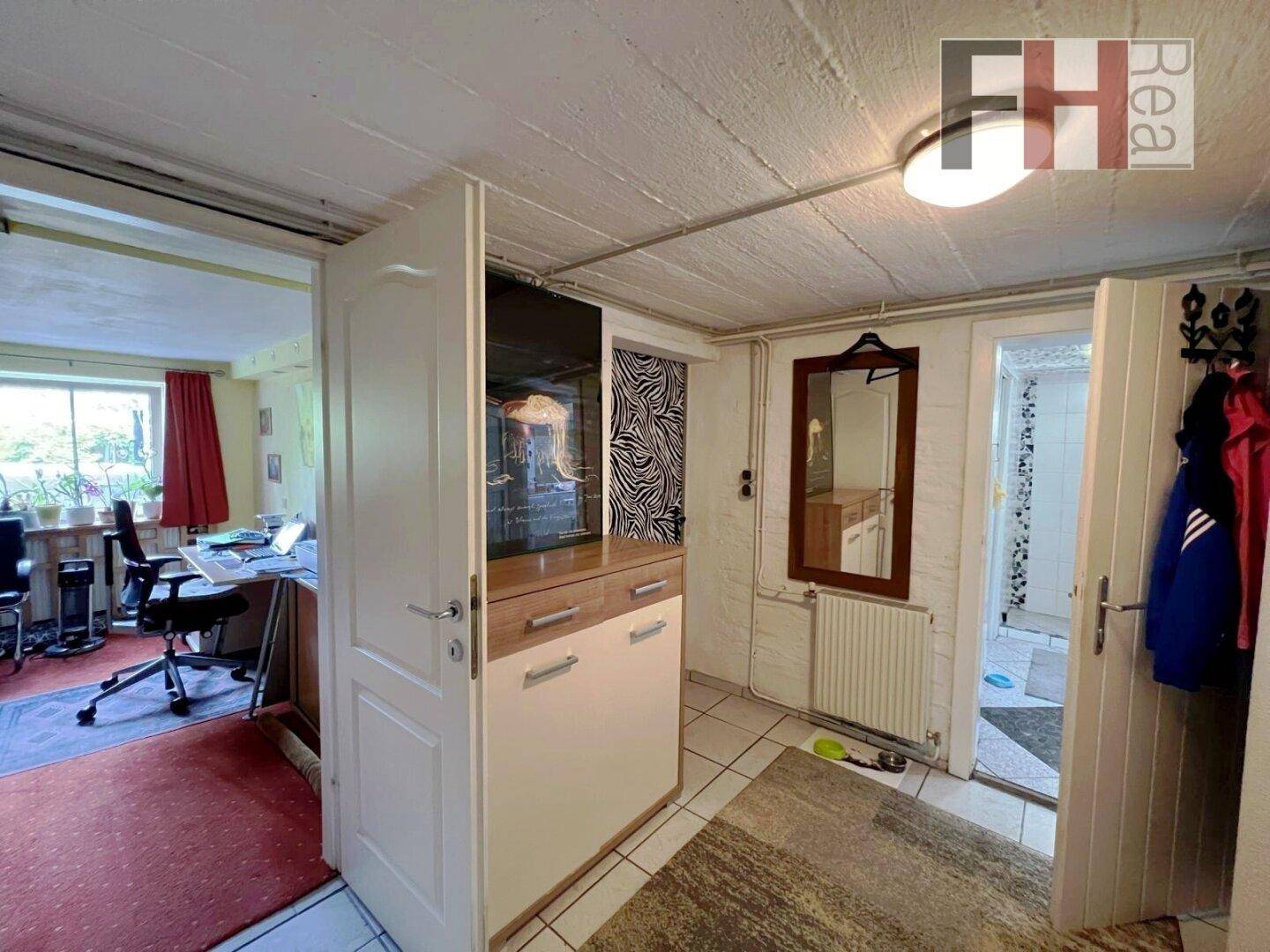Eingangsbereich mit Fliesenboden, Garderobe und Blick in ein angrenzendes Arbeitszimmer mit Fenster.