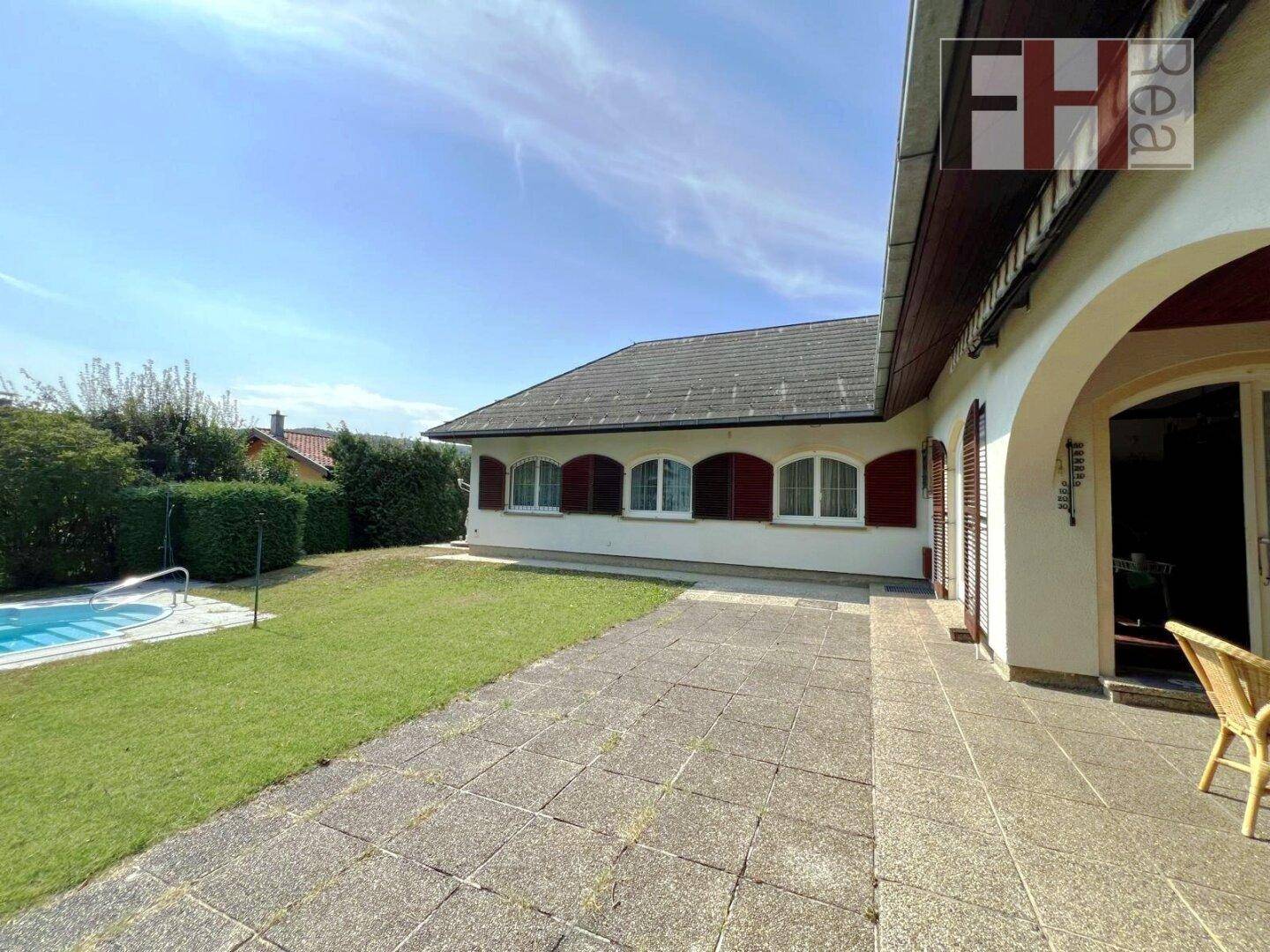 Gepflasterte Terrasse neben dem Haus mit Zugang zum Garten und Blick auf den Poolbereich.