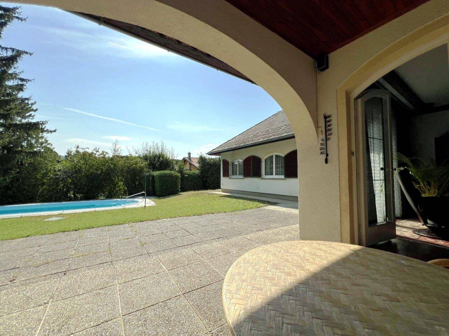Überdachte Terrasse mit Sitzgelegenheiten und direktem Blick auf den Garten und Pool.