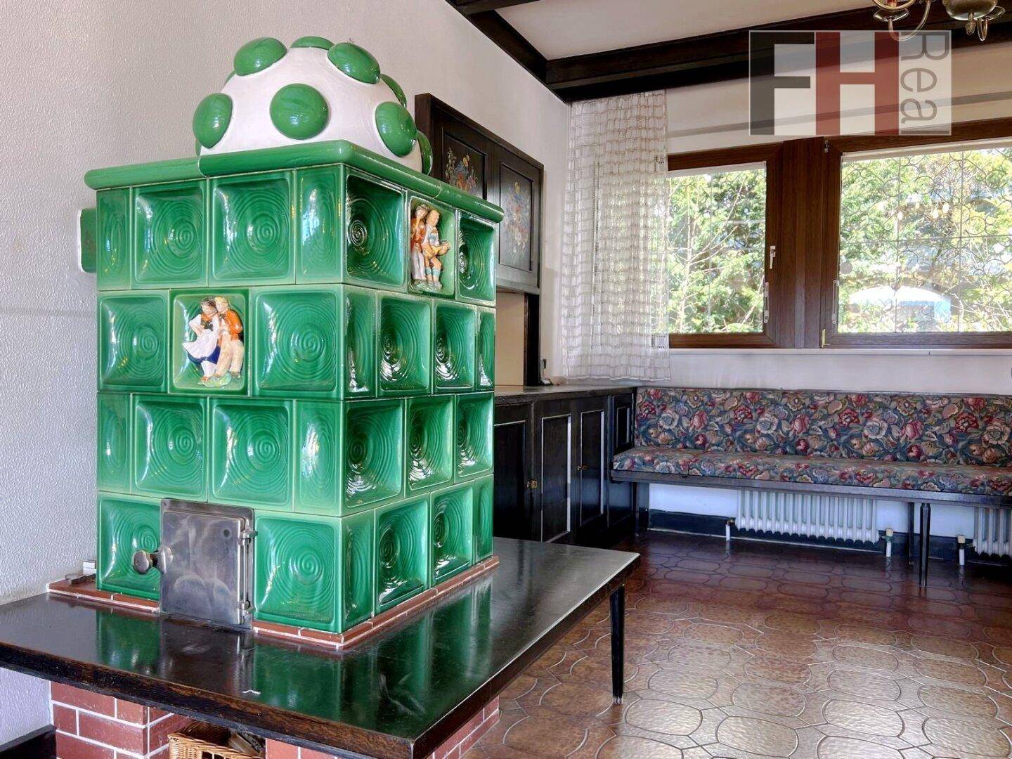 Gemütlicher Wohnbereich mit traditionellem grünem Kachelofen und integrierter Sitzbank am Fenster.