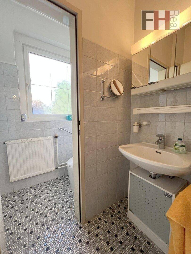 Kleines Badezimmer mit Waschbecken, Toilette und Fenster für natürliche Belüftung.