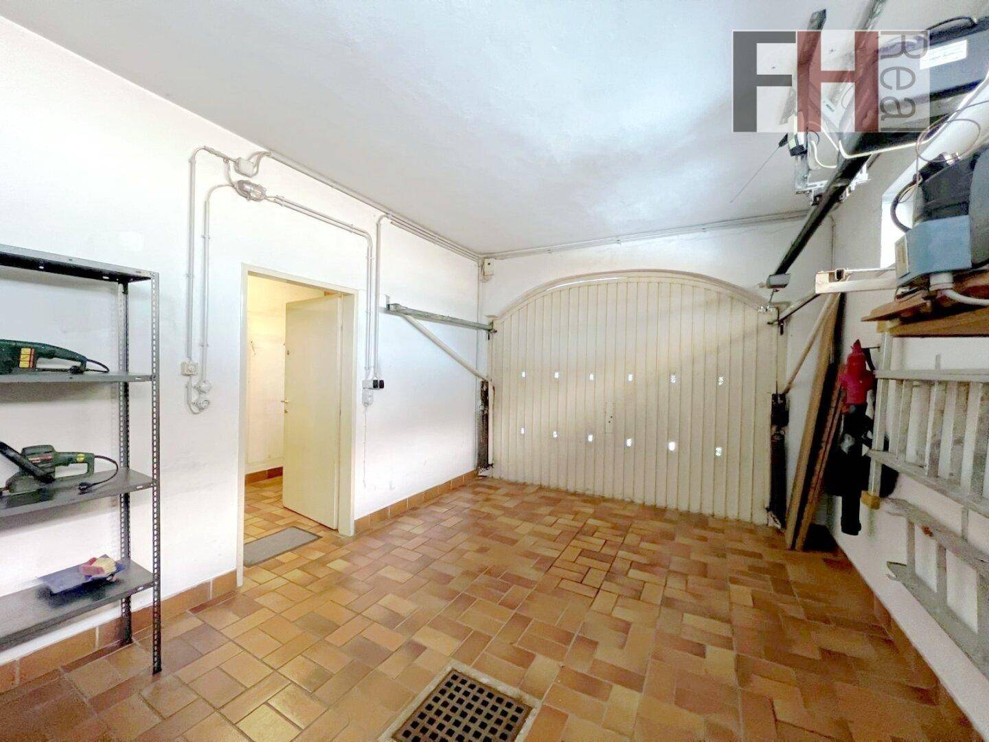 Geräumige Garage mit Fliesenboden, Stauraum und automatischem Tor.