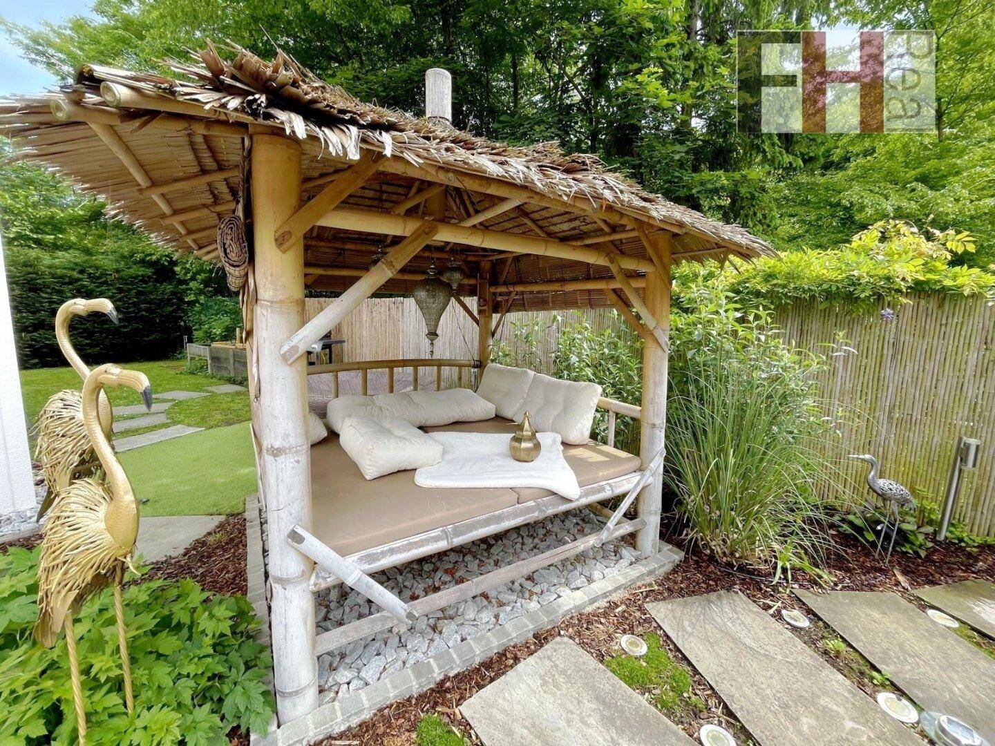 Exotisches Bambus-Gartenpavillon mit bequemer Liegefläche und Strohdach im grünen Garten.