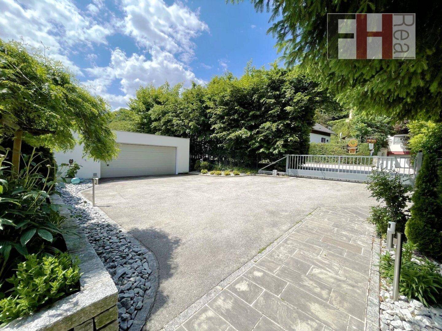 Geräumige Einfahrt mit großer Garage und viel Platz für Fahrzeuge, umgeben von Grün.