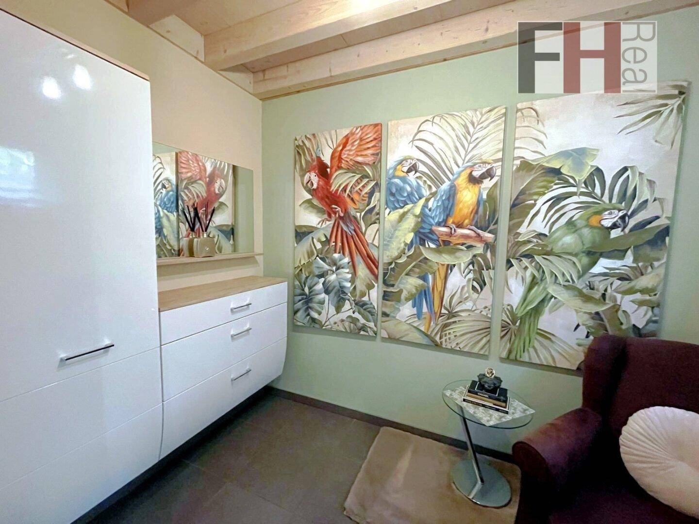 Schlafzimmer mit tropischen Wandbildern, weißem Kleiderschrank und Holzbalkendecke.