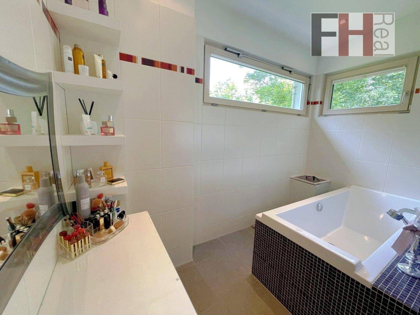 Modernes Badezimmer mit Badewanne, weißen Fliesen und zwei Fenstern für viel Licht.