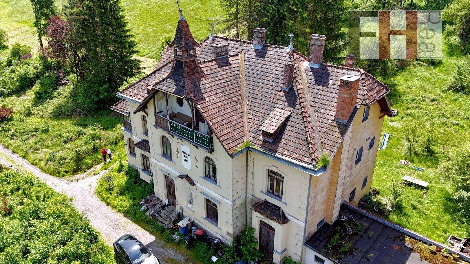 Nahaufnahme des historischen Gebäudes von oben, umgeben von viel Grün und Bäumen.