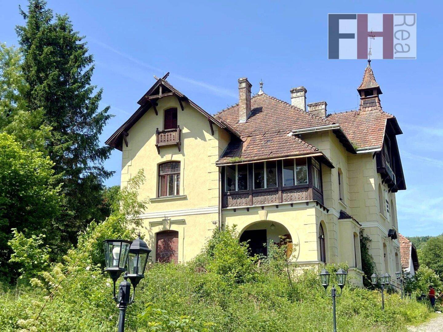 Historisches Gebäude mit gelber Fassade, umgeben von üppiger Vegetation unter blauem Himmel.