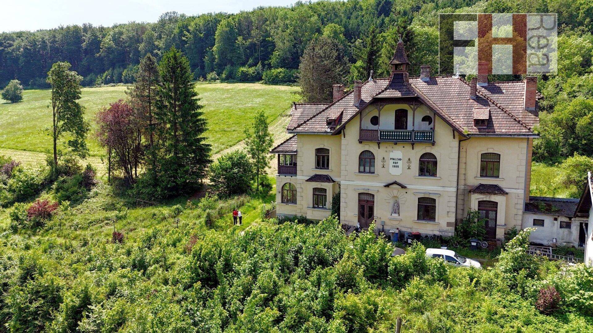 Historisches Anwesen von oben, eingebettet in eine grüne Hügellandschaft mit Wald.