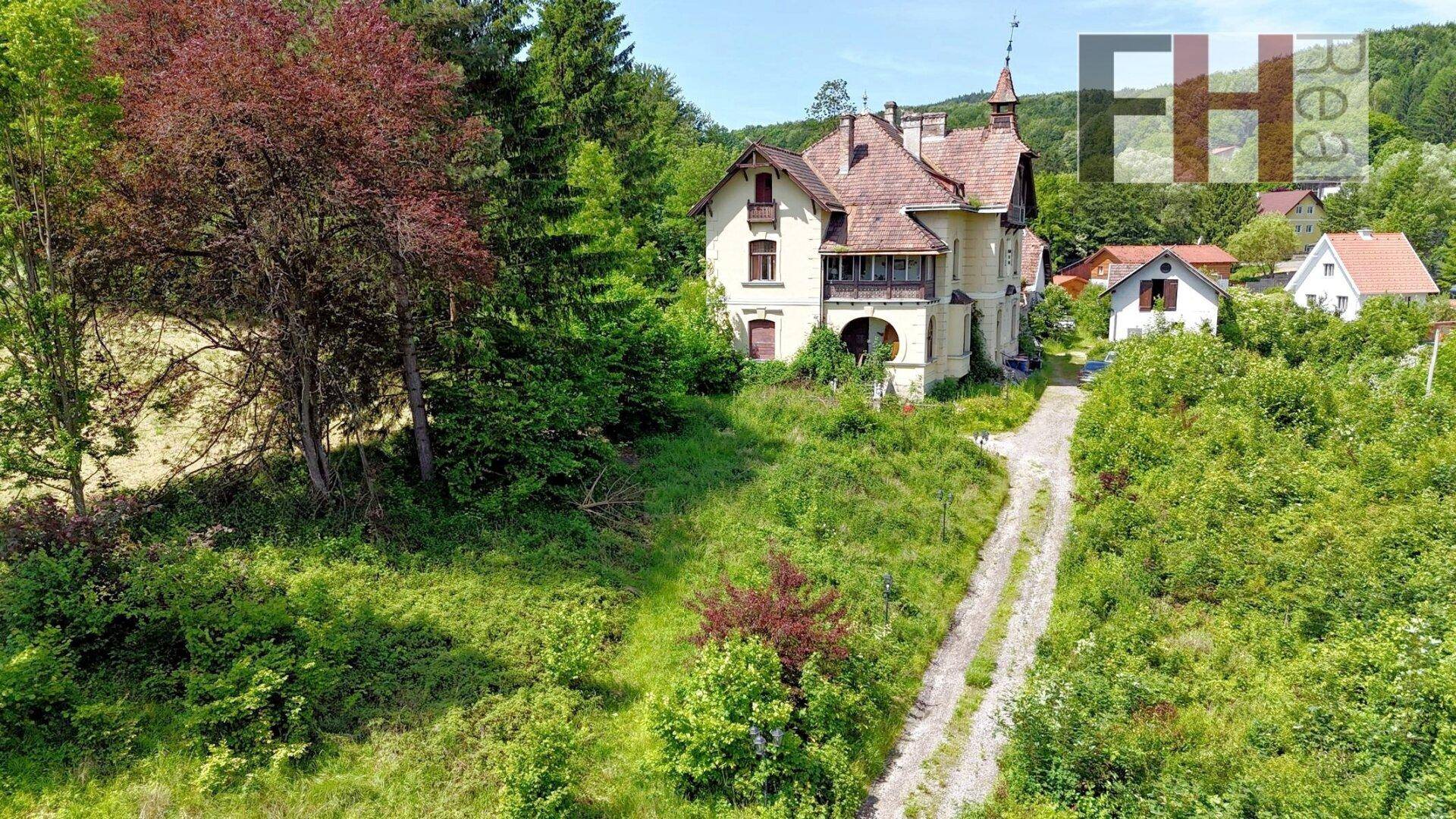 Historisches Gebäude von einem Feldweg aus gesehen, umgeben von Bäumen und Sträuchern.