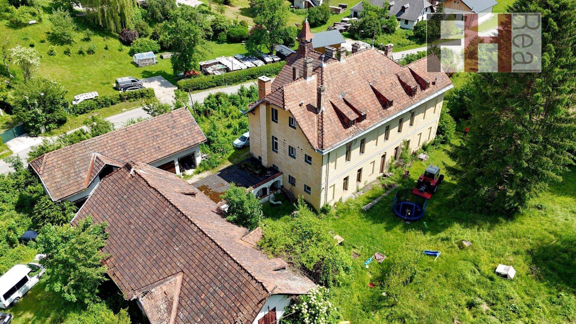 Luftaufnahme des historischen Anwesens mit Nebengebäuden und Blick auf das nahegelegene Dorf.
