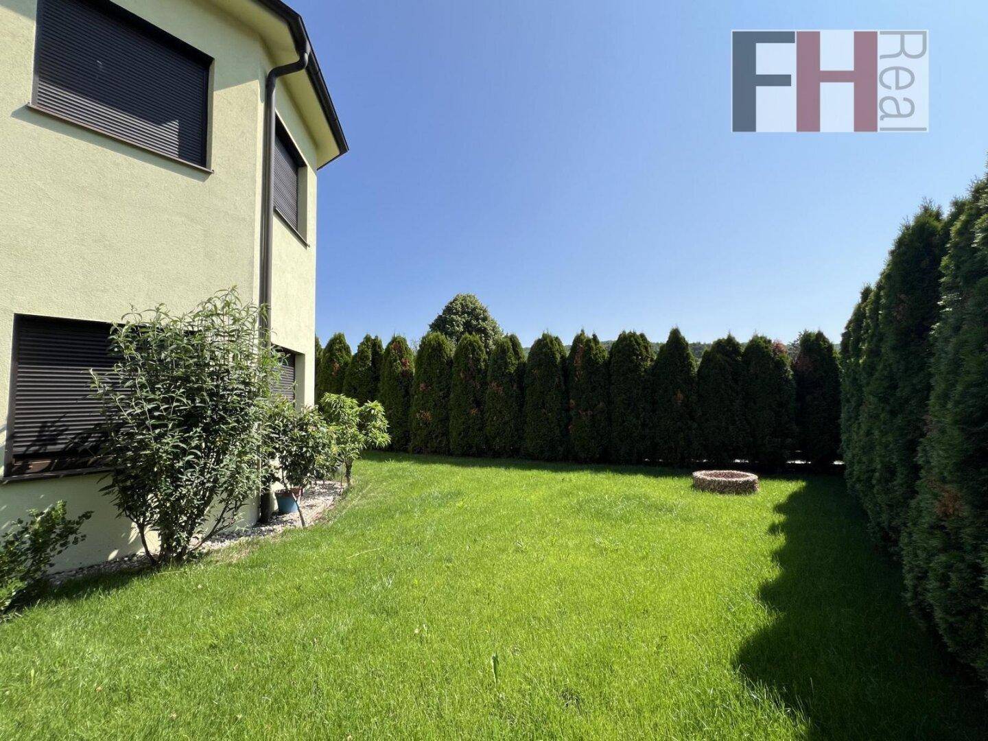 Grüner Rasenbereich im Garten mit hoher Hecke und einer Feuerstelle für gemütliche Abende.