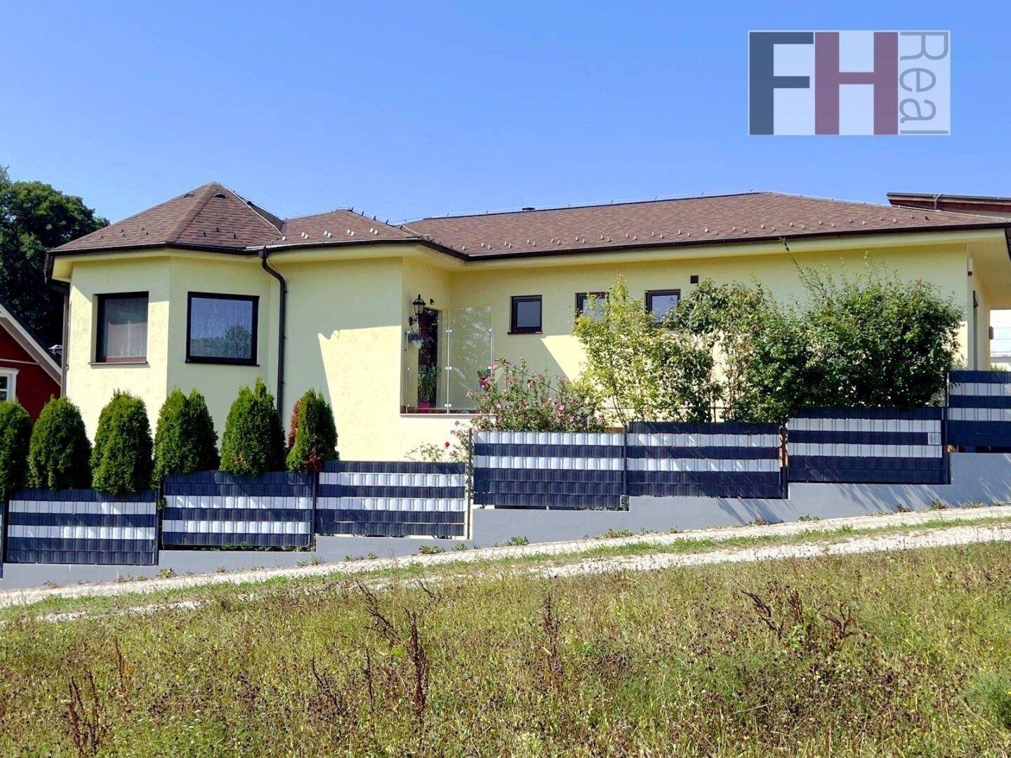 Ansicht der Hausfassade mit gepflegtem Vorgarten und dekorativem Zaun unter blauem Himmel.