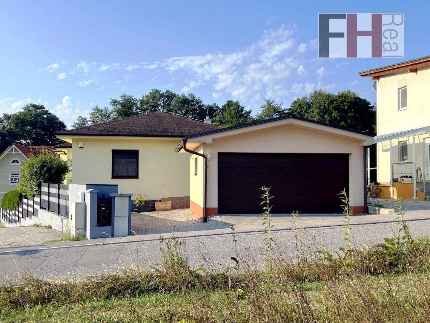 Freistehende Garage mit dunklem Tor und angrenzendem Haus, eingebettet in eine grüne Umgebung.