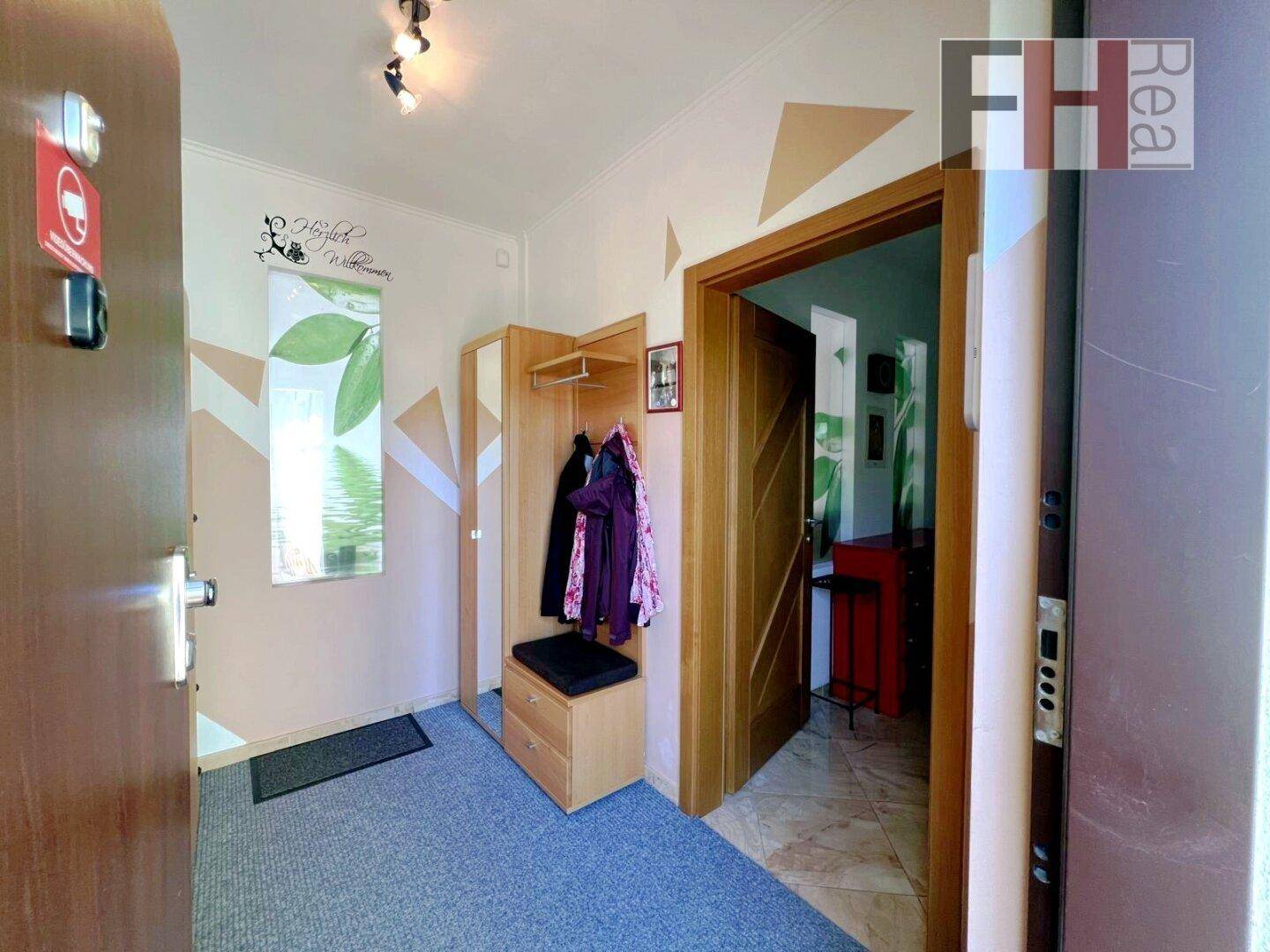 Heller Eingangsbereich mit Garderobe, Spiegel und gemustertem Teppichboden, einladend gestaltet.