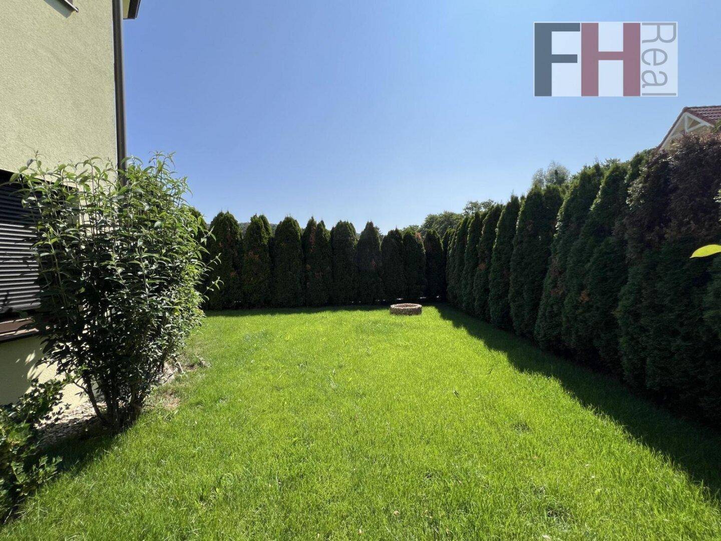 Gepflegter Rasenbereich im Garten, umgeben von einer dichten Hecke und einer kleinen Feuerstelle.