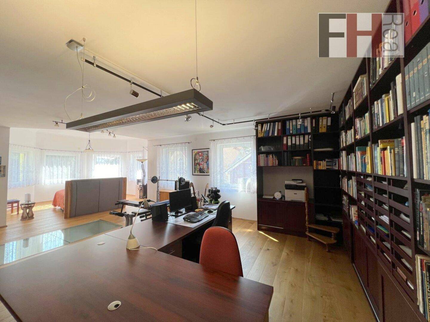 Großzügiges Arbeitszimmer mit umfangreichen Bücherregalen, großem Schreibtisch und Holzfußboden.
