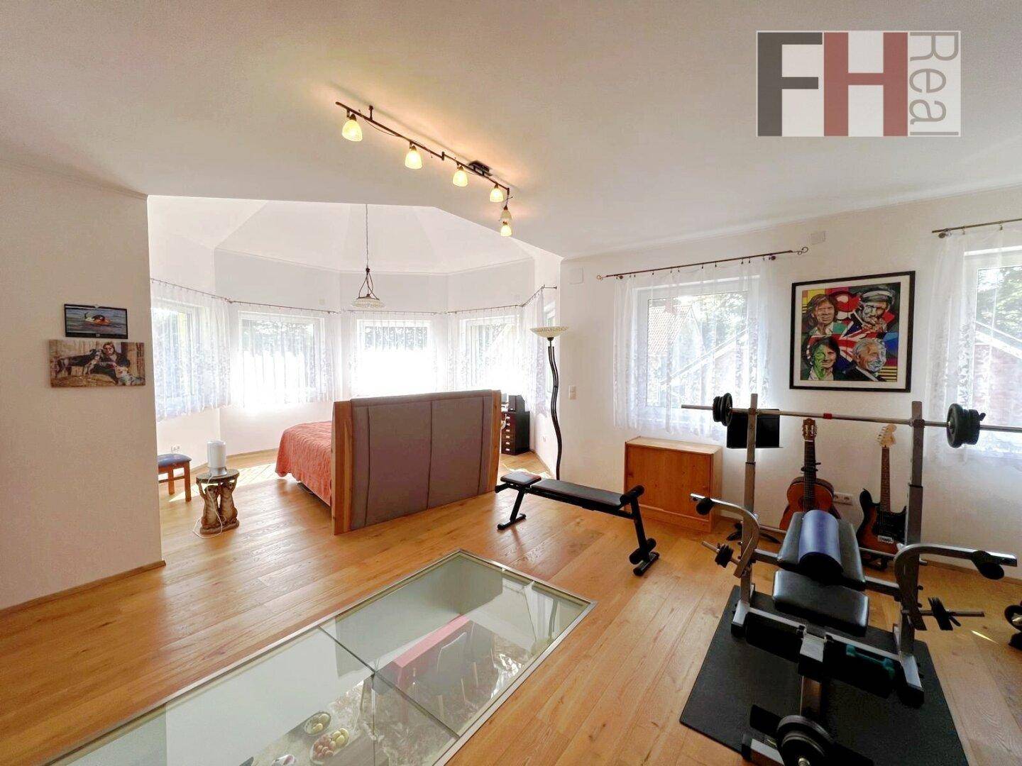 Geräumiges Schlafzimmer mit Bett, Fitnessgeräten, Holzfußboden und vielen Fenstern für viel Licht.