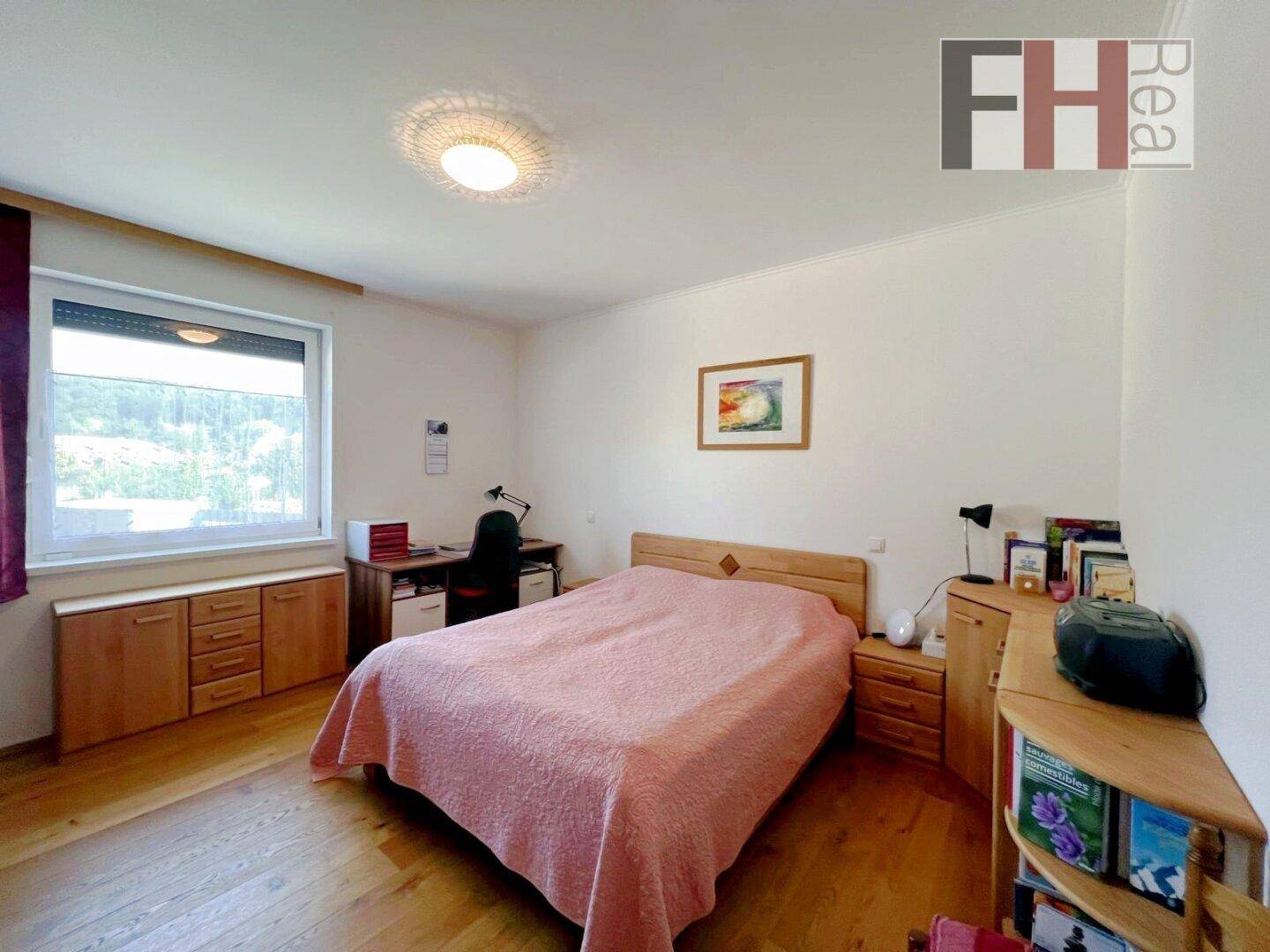Gemütliches Schlafzimmer mit Bett, Schreibtisch, Holzfußboden und einem Fenster mit Rollladen.