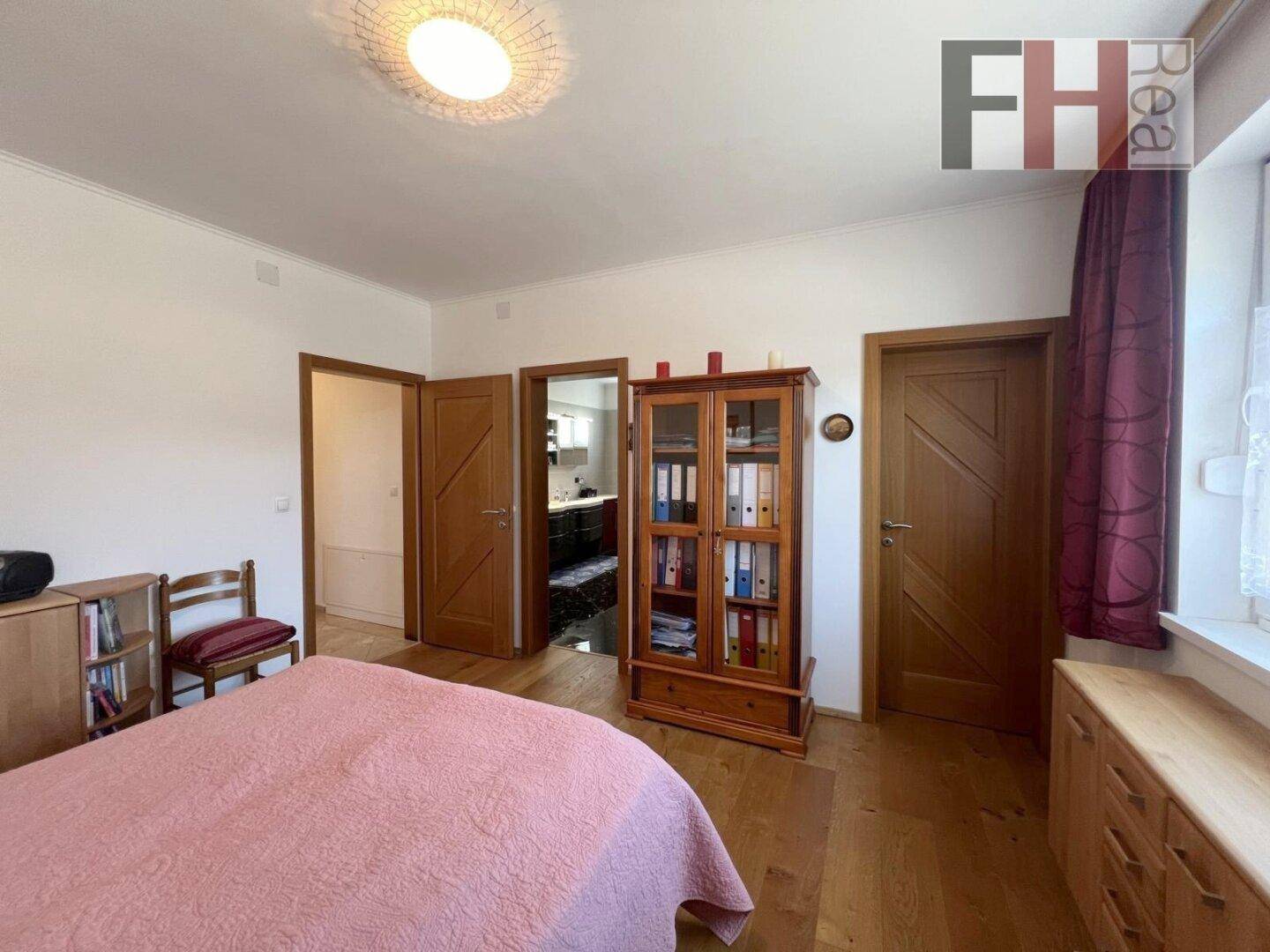 Schlafzimmer mit Holzfußboden, einem Bett und Türen, die zu angrenzenden Räumen führen.
