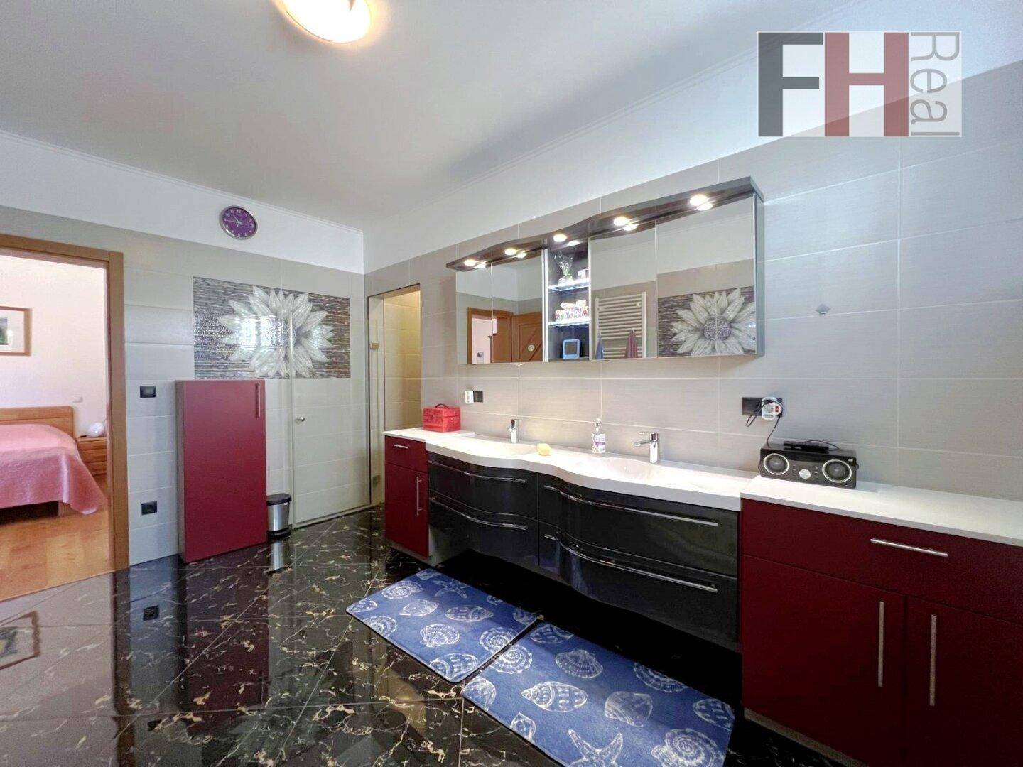 Elegantes Badezimmer mit großem Doppelwaschbecken, Spiegelschrank und dunklem Fliesenboden.