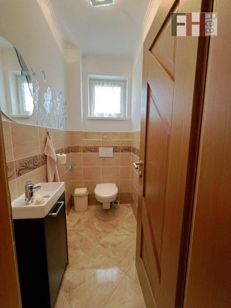 Kleines Gäste-WC mit Fenster, Waschbecken, Toilette und beigefarbenen Wandfliesen.