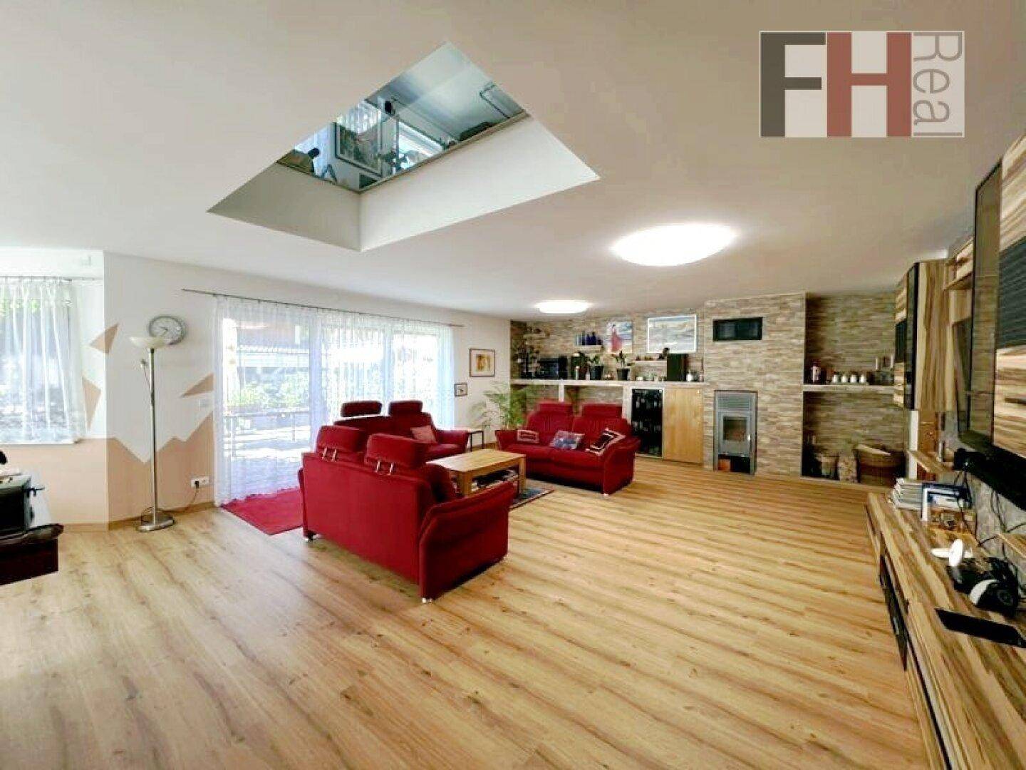 Geräumiges Wohnzimmer mit roten Sofas, Laminatboden, großen Fenstern und Kaminofen.