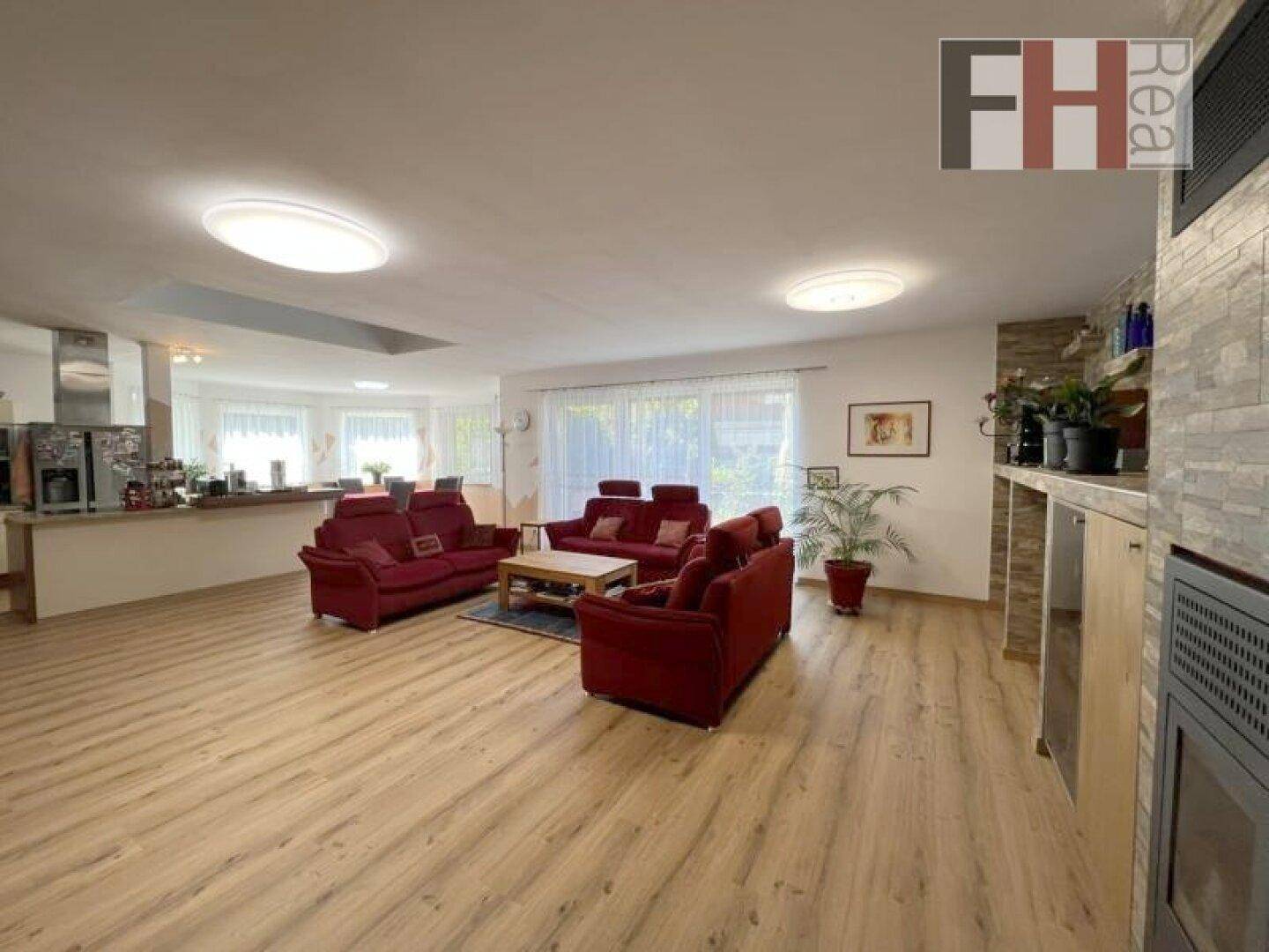 Geräumiger offener Wohnbereich mit bequemen roten Sofas, Laminatboden und Blick zur Küche.