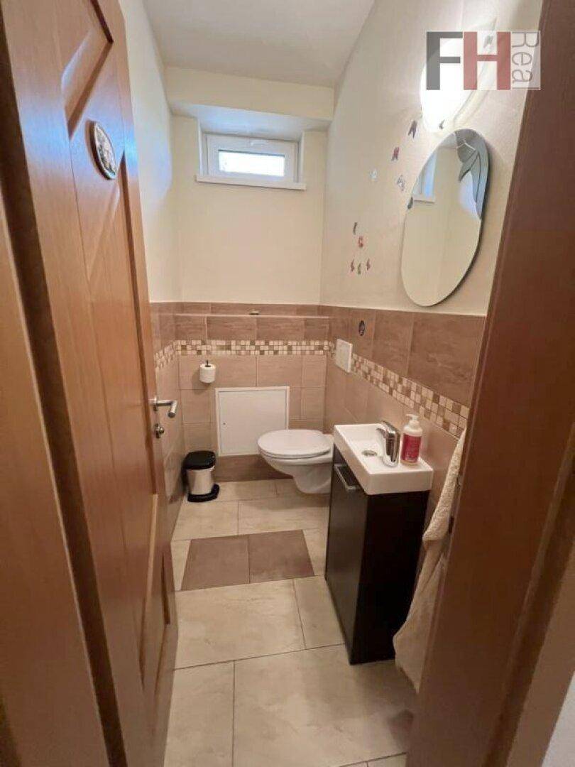Helles Gäste-WC mit Fenster, Waschbecken, Toilette und beigefarbenen Fliesen.