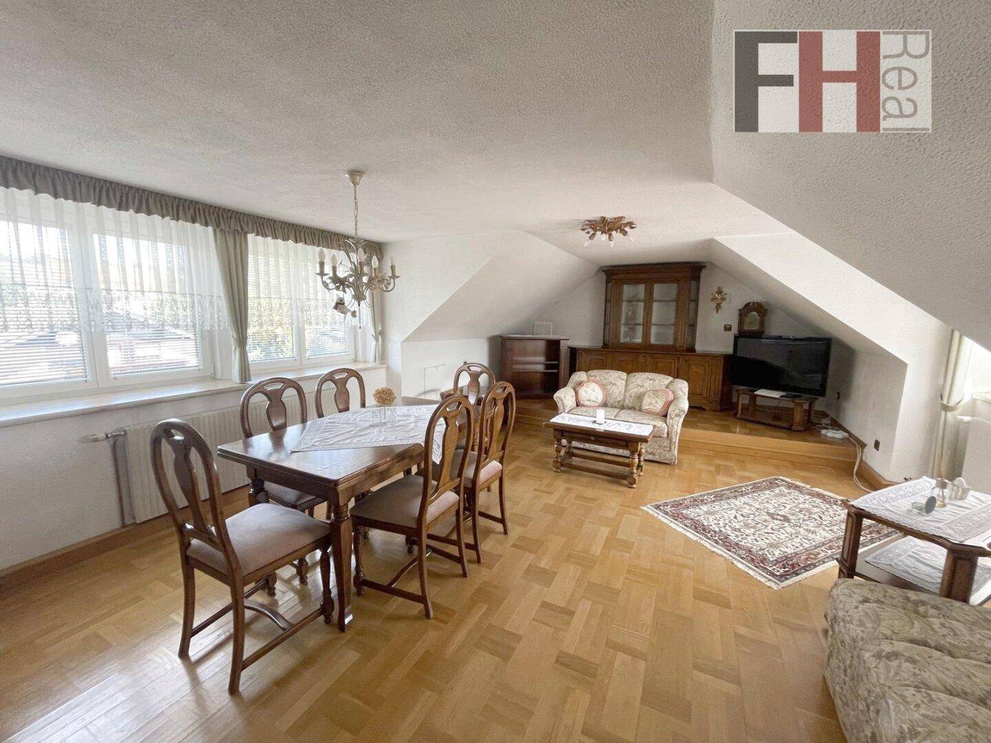 Gemütlicher Wohn- und Essbereich im Dachgeschoss mit Holzboden und schrägen Wänden.