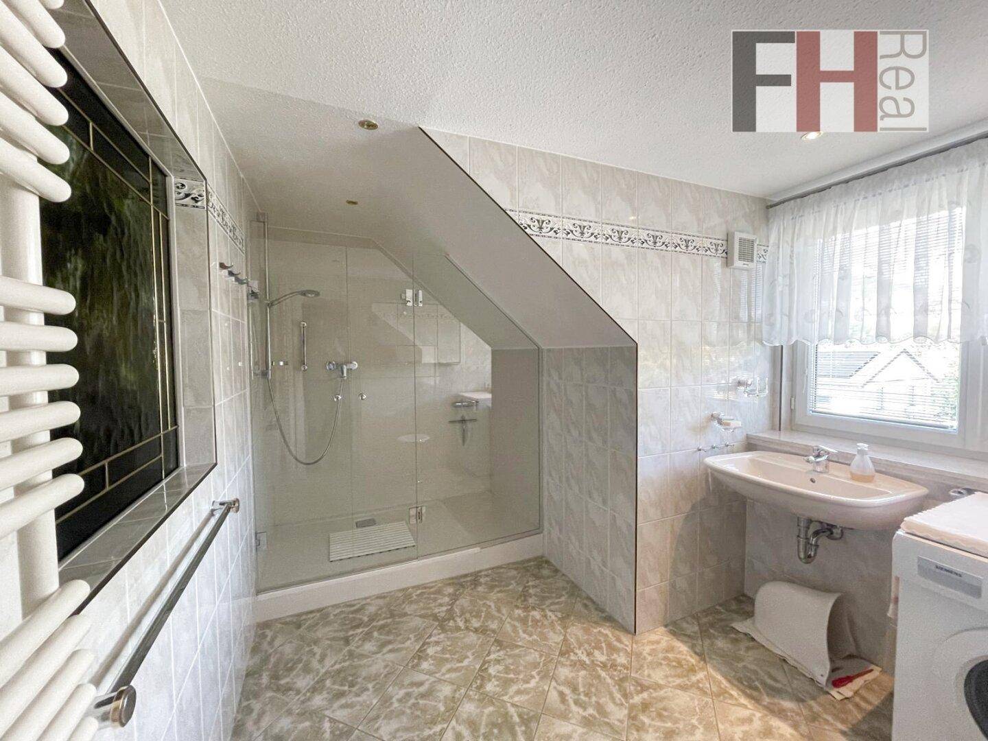 Gefliestes Badezimmer im Dachgeschoss mit Dusche, Waschbecken und beheiztem Handtuchhalter.