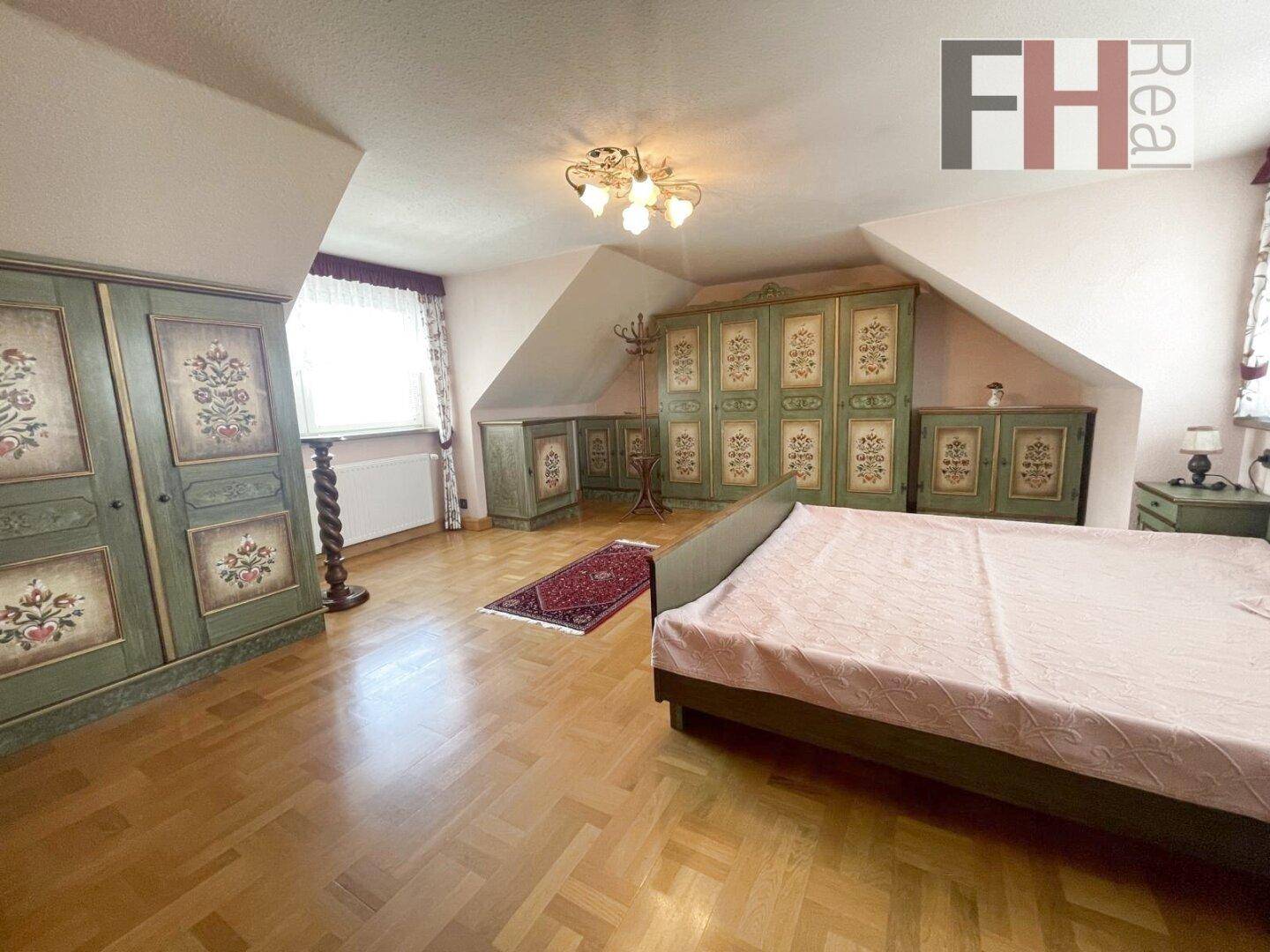 Schlafzimmer mit Holzboden, traditionellen bemalten Schränken und Dachschräge.