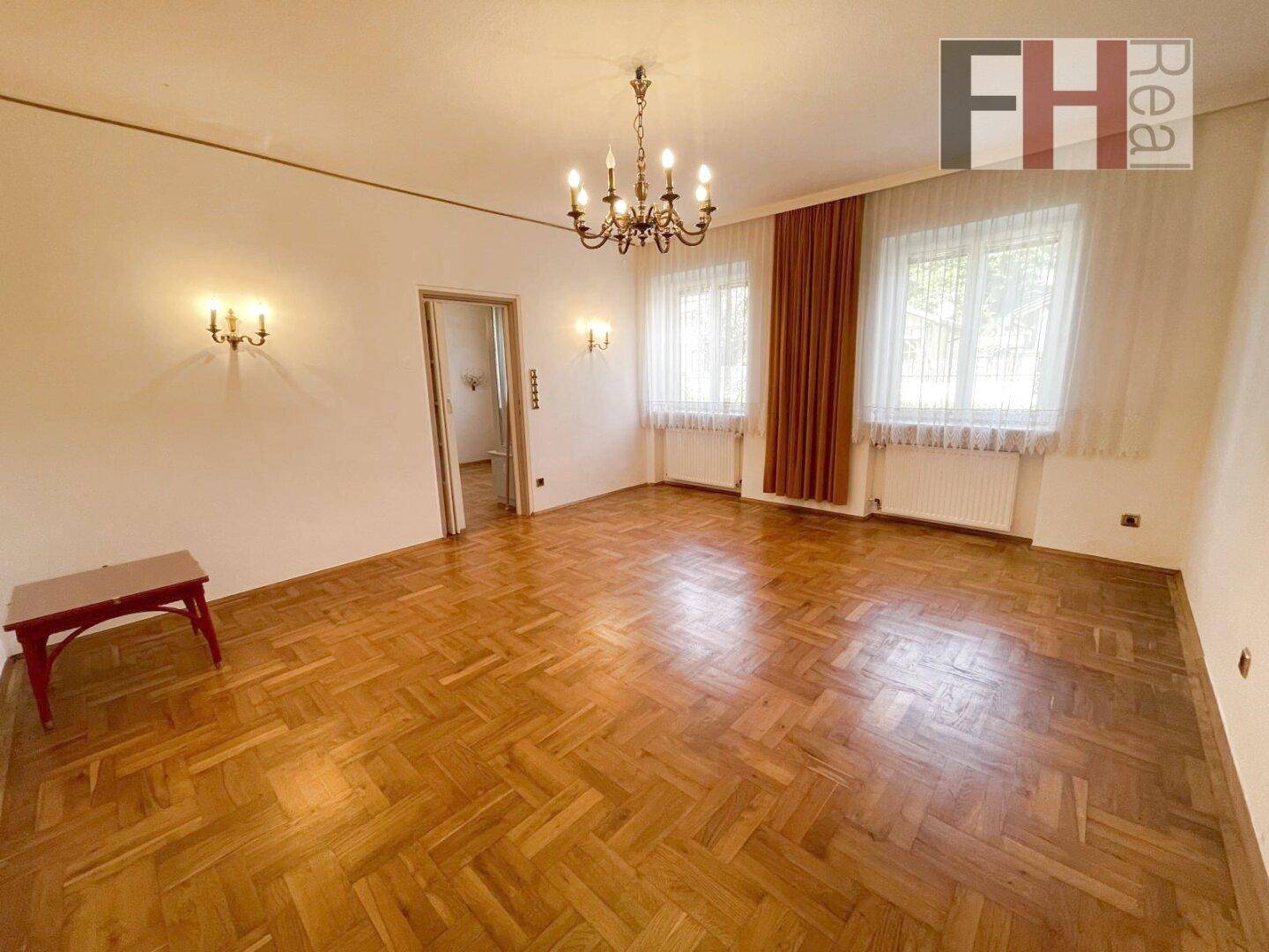 Geräumiges Wohnzimmer mit Parkettboden, Kronleuchter und großen Fenstern.