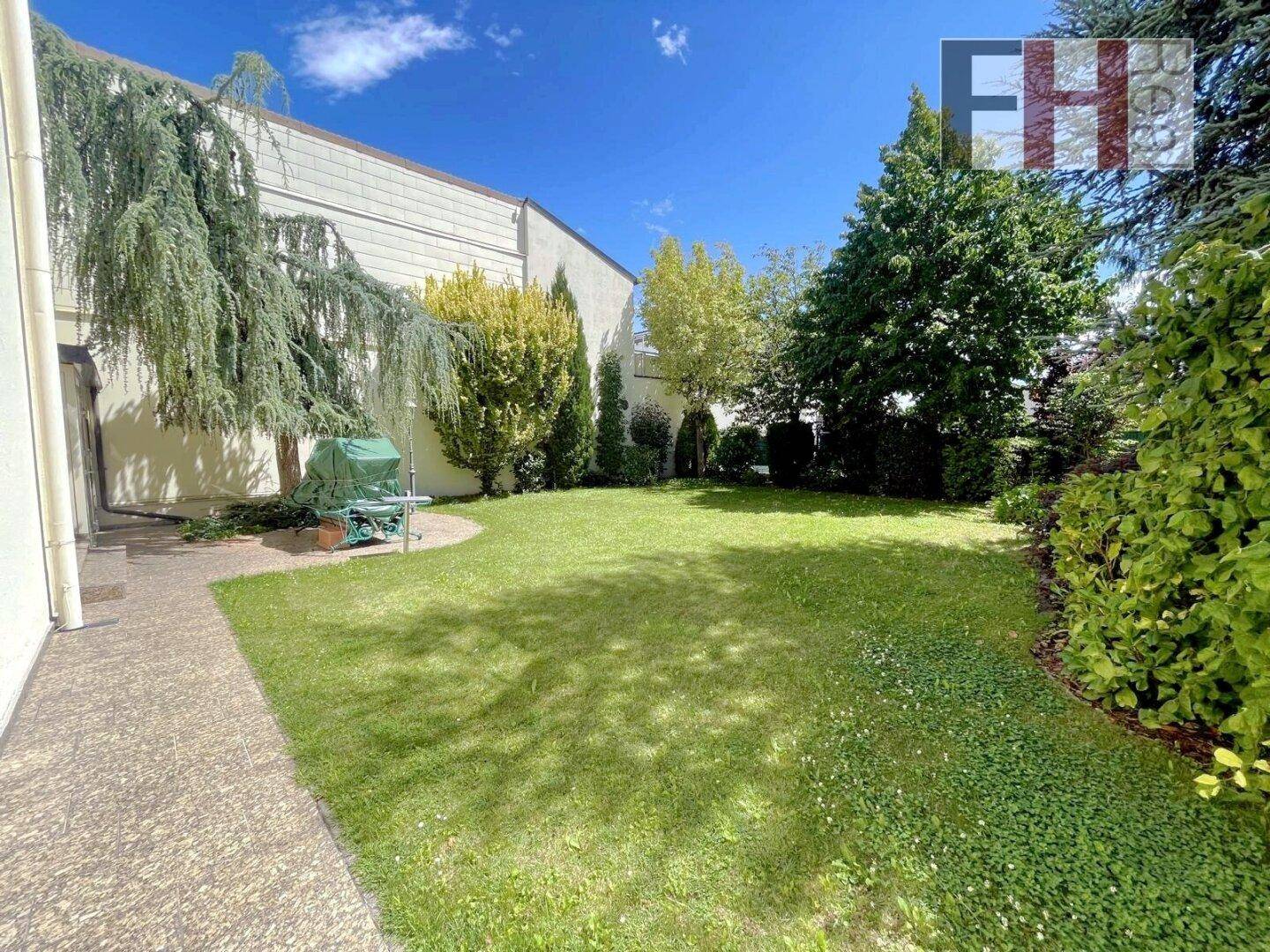 Weitläufiger Garten mit Rasenfläche, hohen Bäumen und einem gepflasterten Weg.
