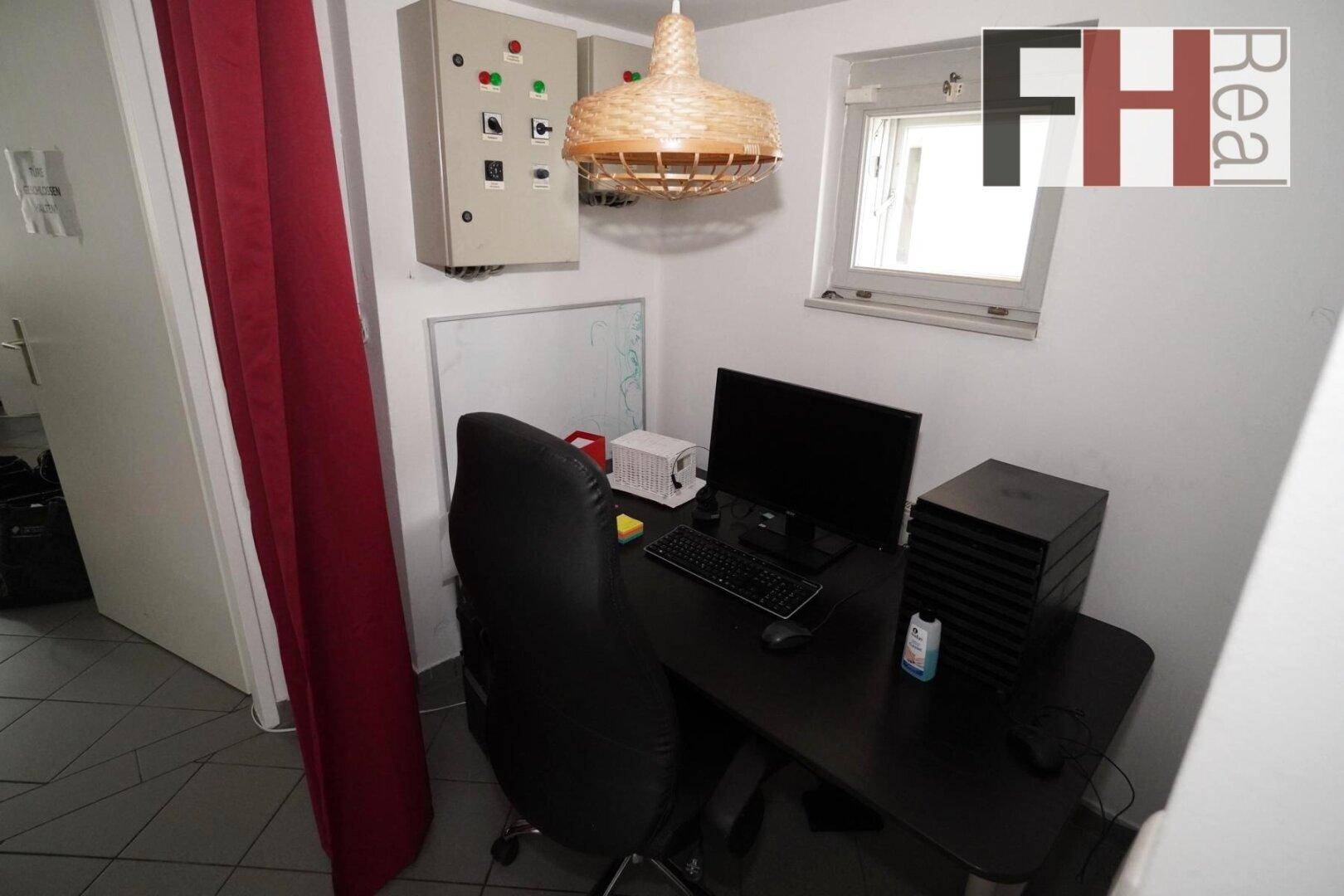 Kleiner Arbeitsbereich mit Schreibtisch, Computer und einem Fenster für Tageslicht.