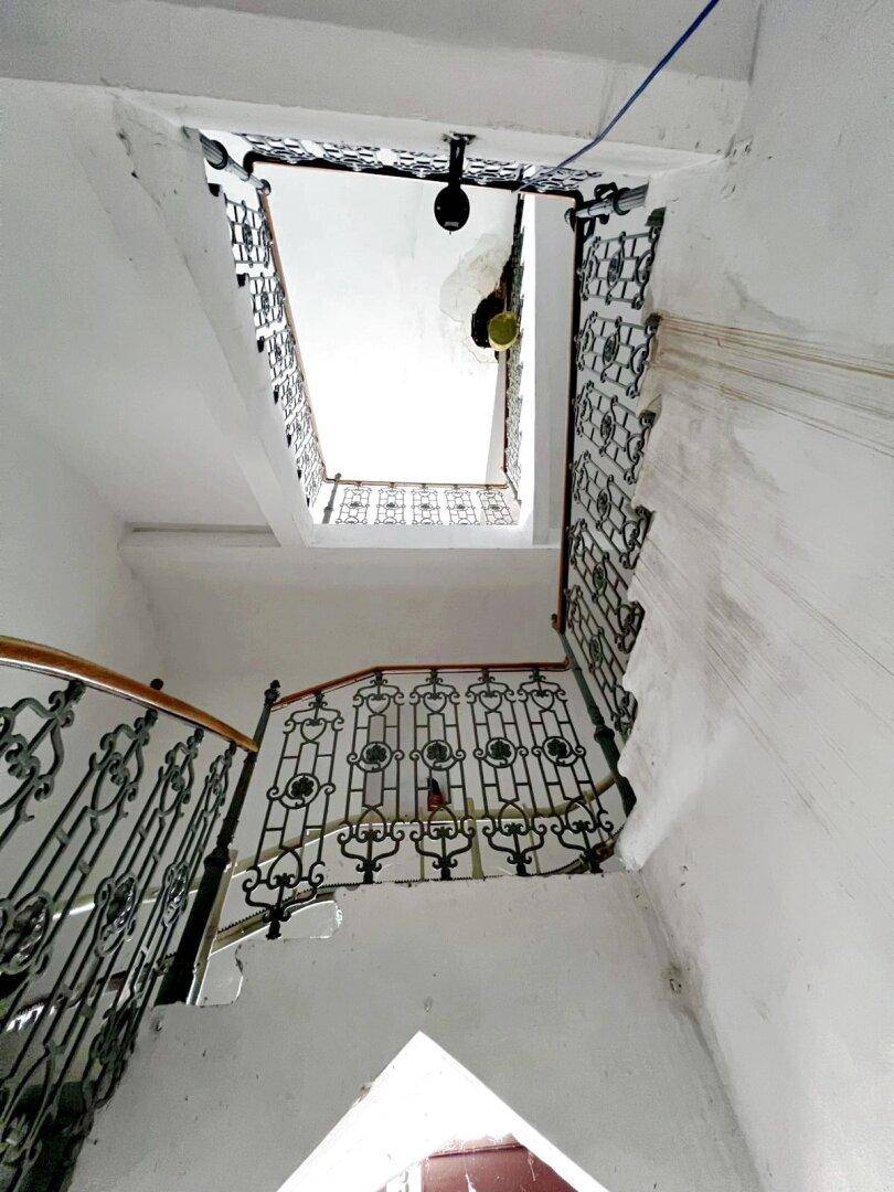Blick nach oben im historischen Treppenhaus mit kunstvollem Geländer und hohen Decken.