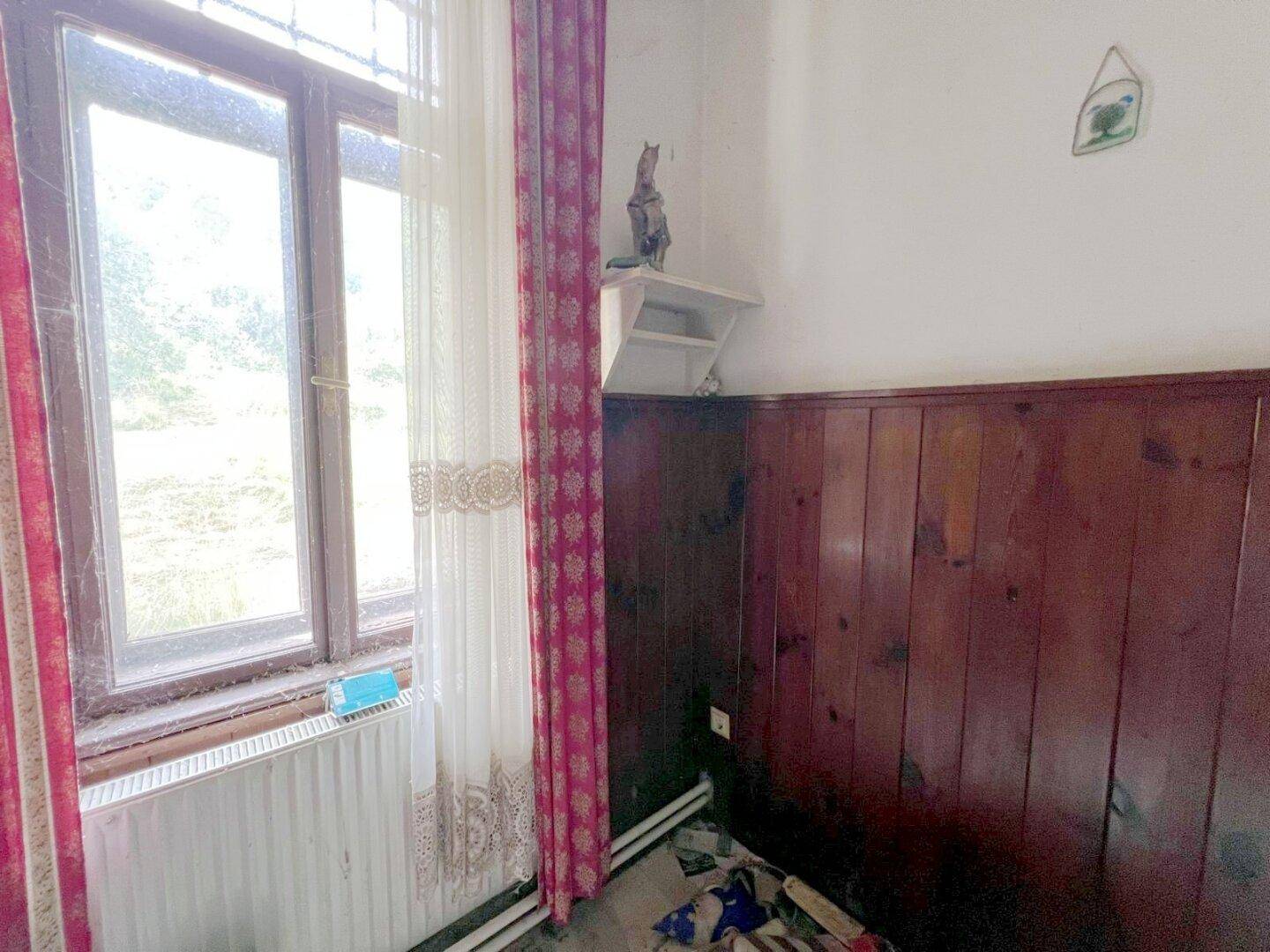 Heller Raum mit Holzvertäfelung, großem Fenster und Blick ins Grüne, ausgestattet mit einem Heizkörper.