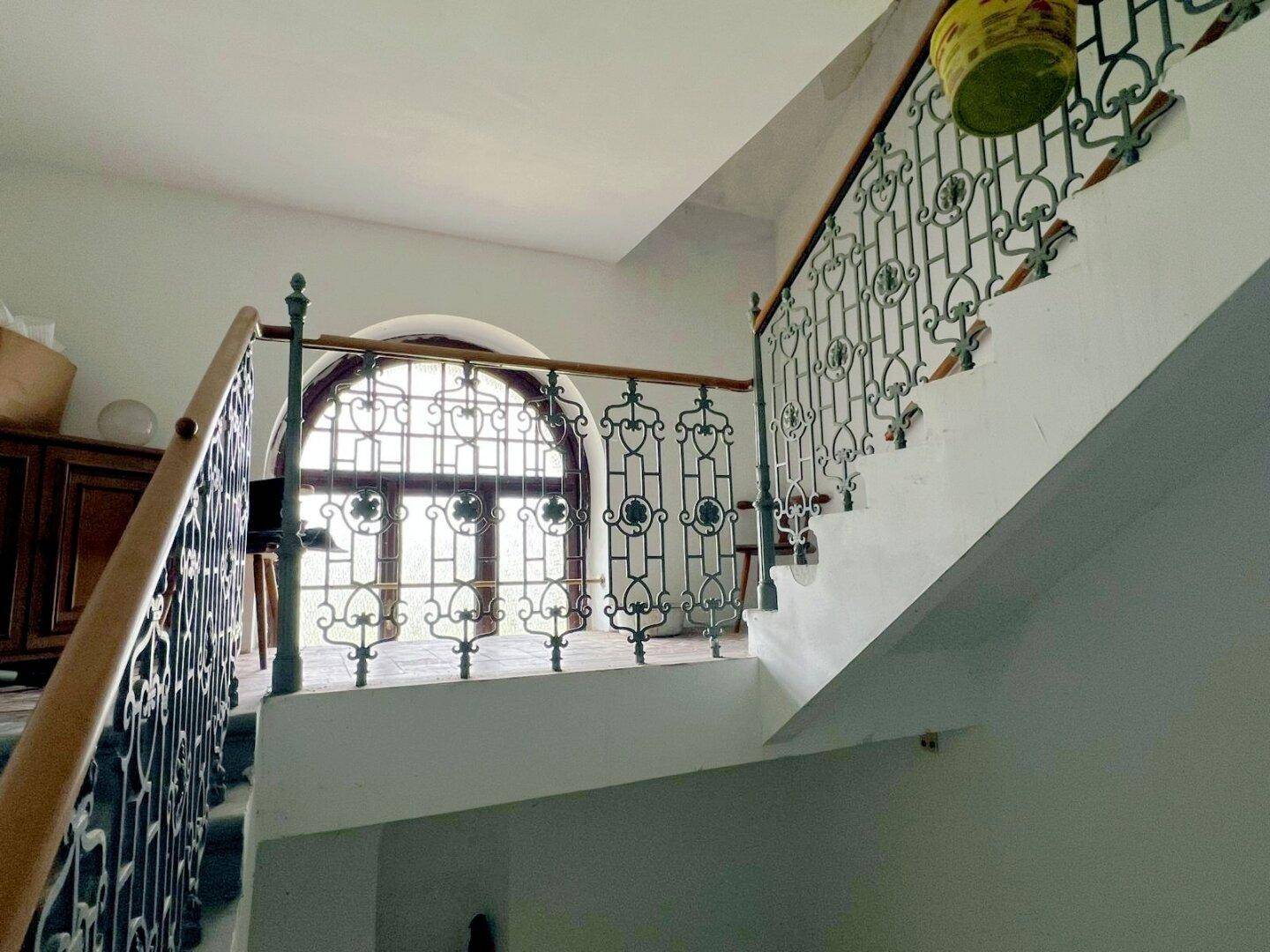 Treppenabsatz mit großem, kunstvoll vergittertem Fenster, das viel natürliches Licht hereinlässt.